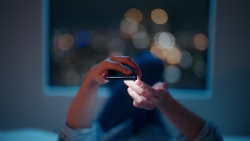 Person using a smartphone in a dimly lit room, highlighting engagement with mobile technology.